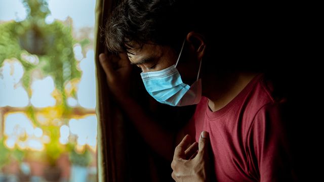 A man wearing a face mask and holding a hand to his chest, as if he is coughing. 