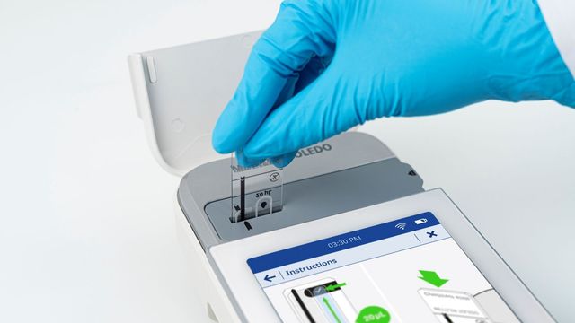 Gloved hand inserting a laboratory slide into a digital slide scanner. 