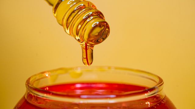 Honey dipper dripping golden honey into a glass container. 