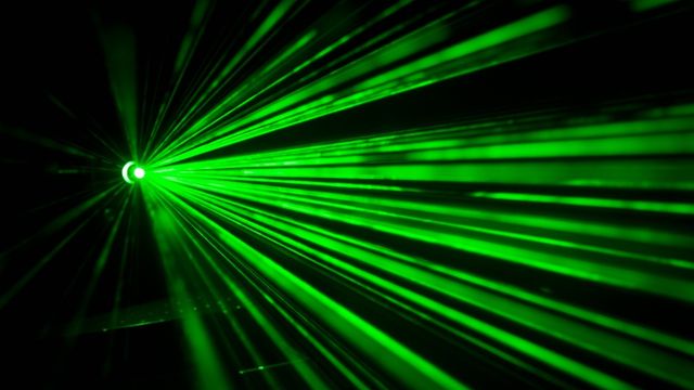 Green laser light beams radiating from a bright point against a black background. 