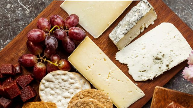 An overhead photograph of a cheeseboard, featuring a selection of different cheeses, grapes, and crackers. 