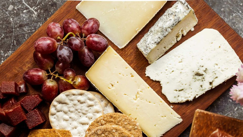 An overhead photograph of a cheeseboard, featuring a selection of different cheeses, grapes, and crackers.