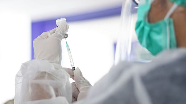 Healthcare professional wearing PPE drawing liquid from a vial into a vaccine needle. 