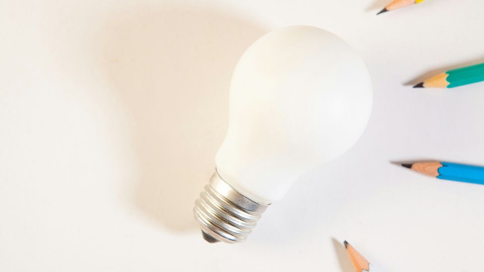 Light bulb surrounded by coloured pencils on a white surface, symbolising thinking and creativity.
