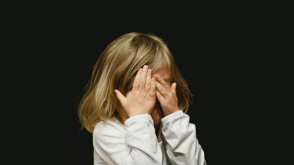 Girl covering her face with her hands against a dark background.