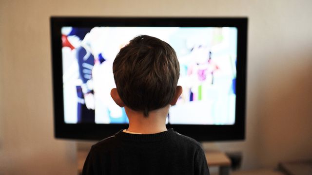 Child viewed from behind watching television in a dim room, illustrating screen time. 