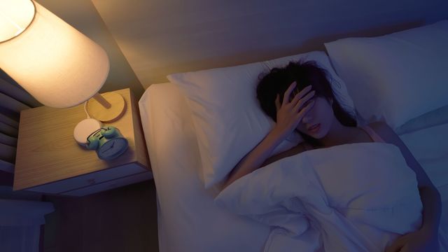 Person lying awake in bed with hand over forehead, illustrating nightmares and disturbed sleep. 