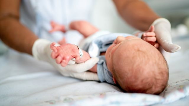 A nurse with gloved hands placing a newborn baby down on a soft surface. 