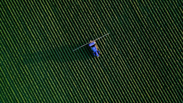 An arial photo of a tractor and farm machinery moving across a field of crops. 