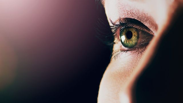 Close-up of an eyeball with detailed green iris, black pupil, and long dark eyelashes. 
