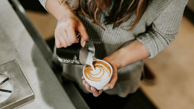 A barista pouring milk into a latte to create a love heart-shaped pattern in the milk. 