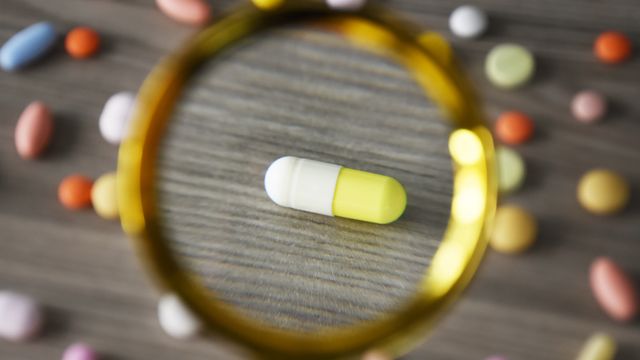 Capsule under a magnifying glass with scattered pills, symbolising drug discovery and pharmaceutical research. 