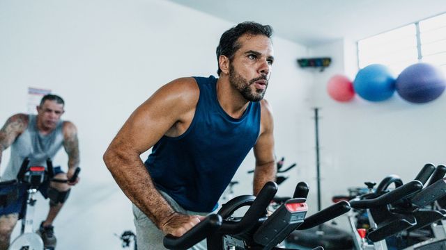 A man in a vest exercises on a piece of gym equipment. 