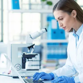 Scientist working with a microscope and laptop in a research lab.