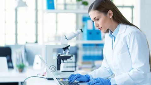 Scientist working with a microscope and laptop in a research lab.