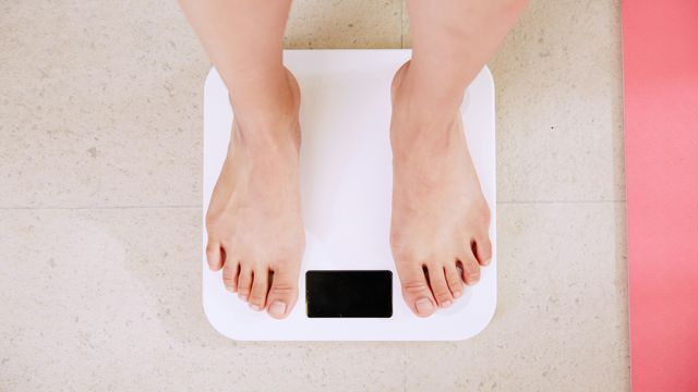 Birds-eye view of feet on a white digital weighing scale. 