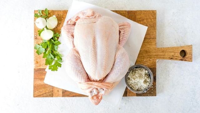 Raw whole chicken on a cutting board with onions, parsley, and coarse salt. 