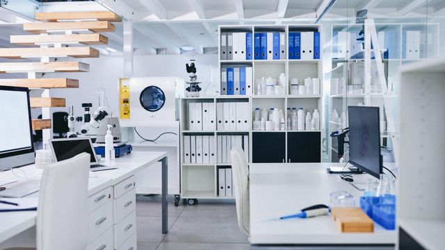 Laboratory containing several pieces of equipment, including a microscope, pipette, conical flasks, reagents in bottles, and computers.  
