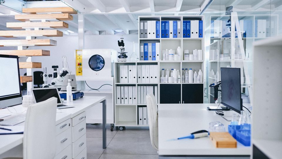 Laboratory containing several pieces of equipment, including a microscope, pipette, conical flasks, reagents in bottles, and computers. 