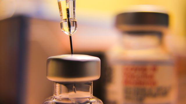A close up of a needle drawing liquid from the top of a vaccine vial. 