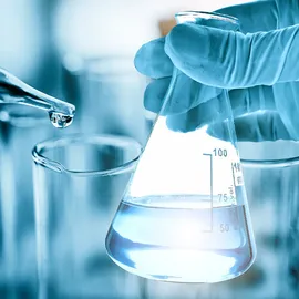 Gloved hand holding a laboratory flask while a pipette dispenses water, illustrating the role of water quality in chemical trace analysis.