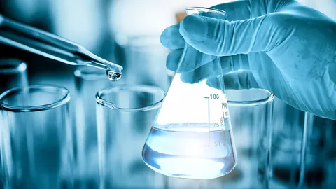 Gloved hand holding a laboratory flask while a pipette dispenses water, illustrating the role of water quality in chemical trace analysis.