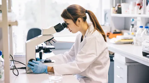 Researcher examining a sample under a microscope for microbial quality control.