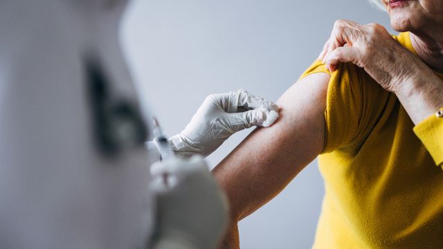 Healthcare worker administering a vaccine injection into an upper arm with a syringe during immunization. 