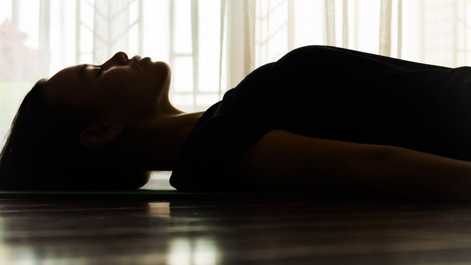 Silhouette of a person lying on a floor beside a sunlit window, often used to illustrate psychedelics research.