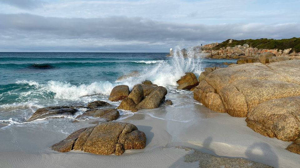 A wave crashing against large rocks on a beach.