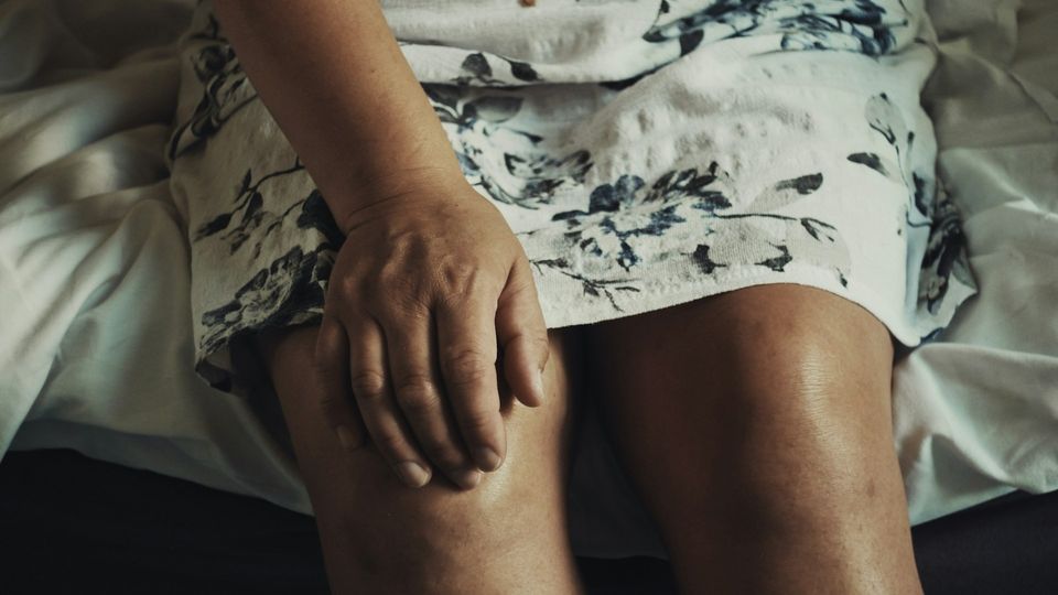 Person holding a painful knee while sitting on a bed.