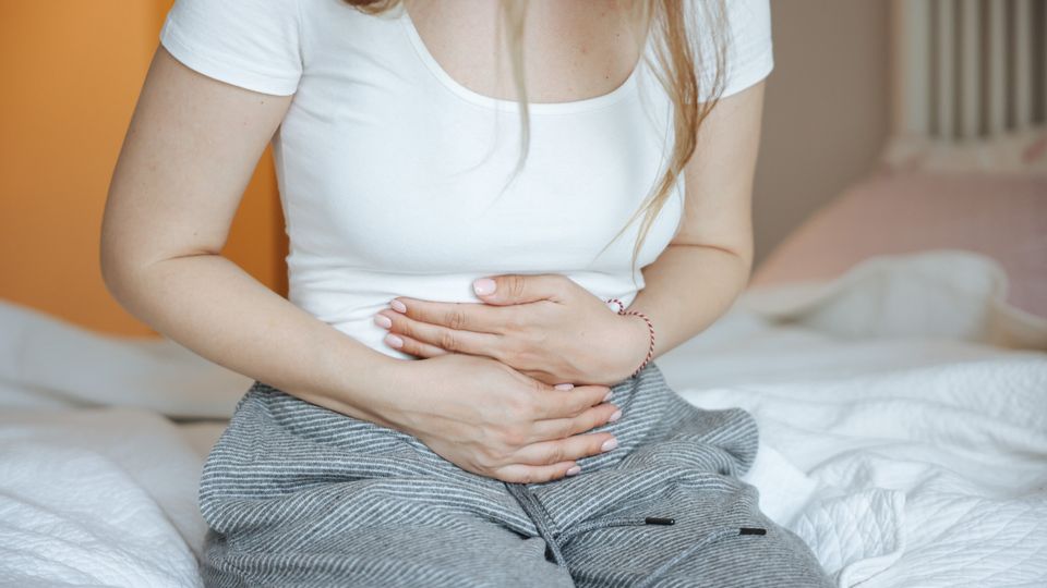 Person sitting on a bed holding their abdomen, illustrating chronic pain and abdominal discomfort.