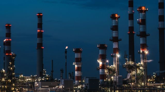 Oil refinery with illuminated industrial processing towers and smokestacks at night. 