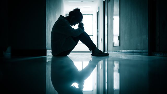Silhouette seated on a hallway floor with head lowered, commonly used to illustrate depression. 