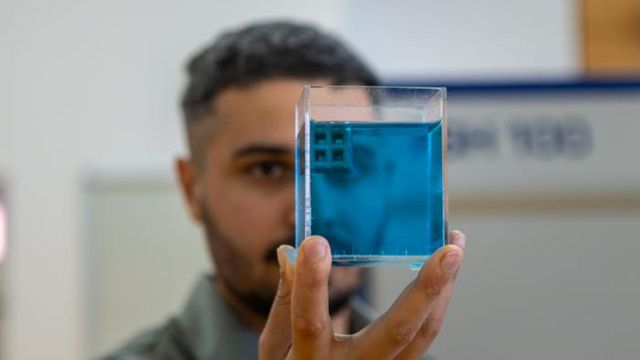 Scientist holding a blue titanium sample in a laboratory. 