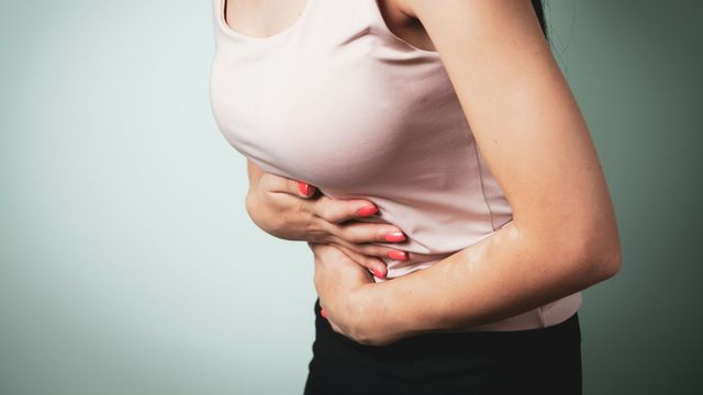 Close-up of a person's mid-section as they hold their stomach in pain. 