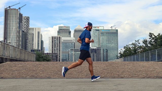 Man running on a city bridge with London skyscrapers in the background. 