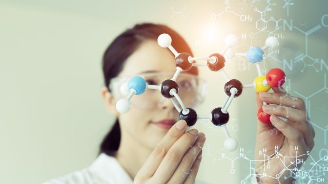 A researcher holding up a stick-and-ball model of a large molecule 