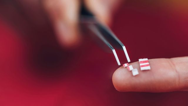 Tweezers placing small blotter paper tabs on a fingertip, representing LSD dosage forms. 