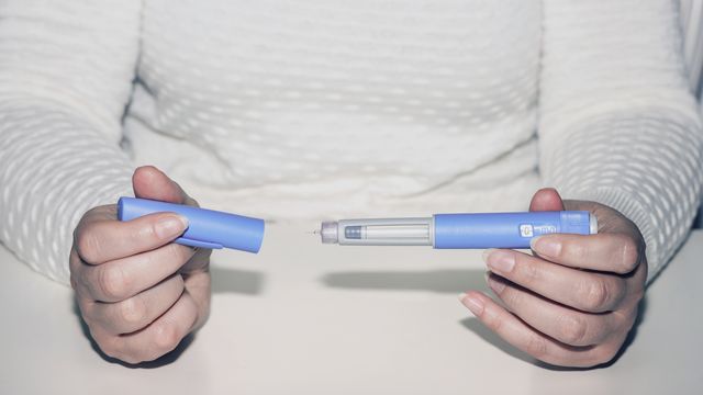 Close-up of a person's hands removing the lid from a GLP-1 injection pen. 