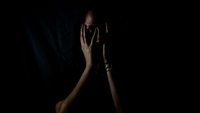 Girl covering her face in a dark setting, conveying fear or distress. 