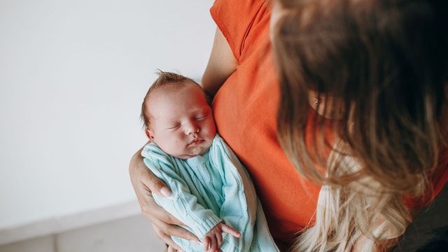 Mother holding a sleeping newborn baby in a light blue sweater. 