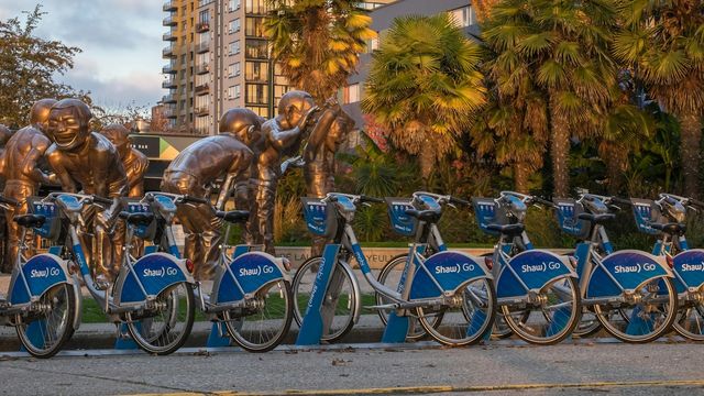 City bike-sharing bicycles parked at a docking station near a public sculpture. 