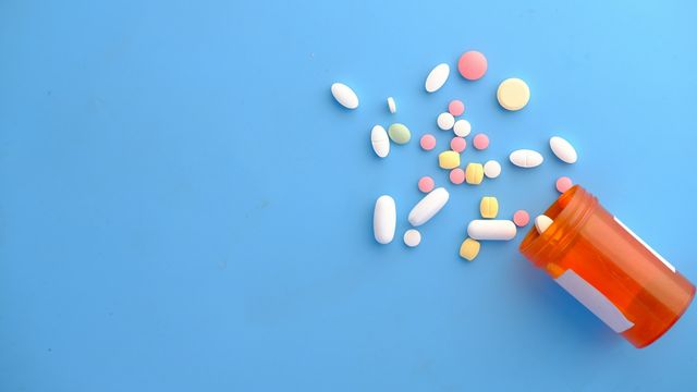 Prescription pills spilling from an orange medicine bottle onto a blue background. 