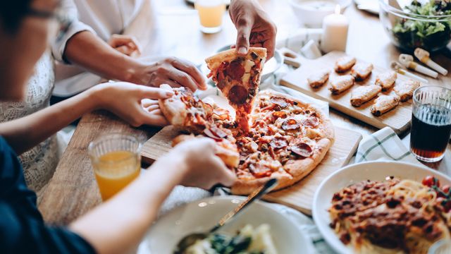 People reaching for pizza from a restaurant table.  