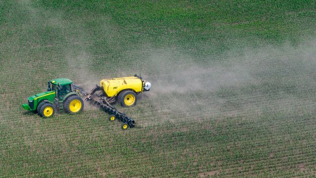 A tractor pulls a container of pesticide across a field, spraying as it goes. 