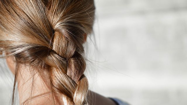 Blonde hair tied into a braid seen from the back of a woman's head.  