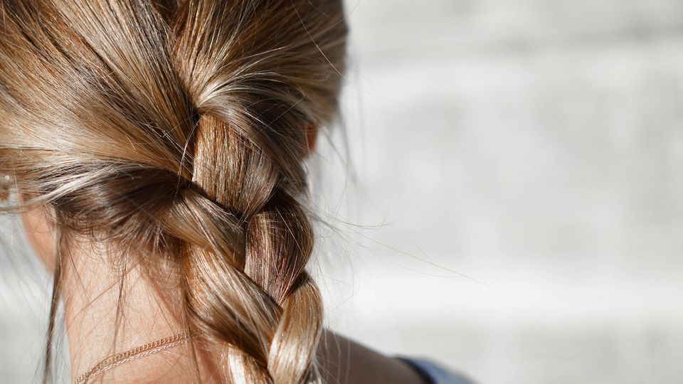 Blonde hair tied into a braid seen from the back of a woman's head. 
