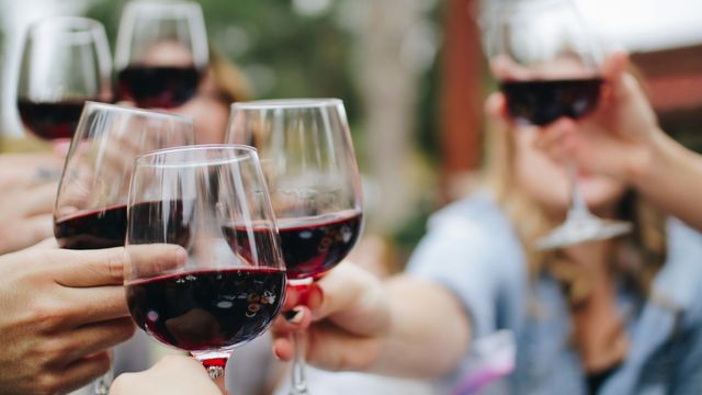 People holding glasses of red wine at a gathering. 
