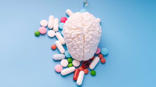 Birds-eye view of a brain model surrounded by an assortment of pills, on a blue surface. 